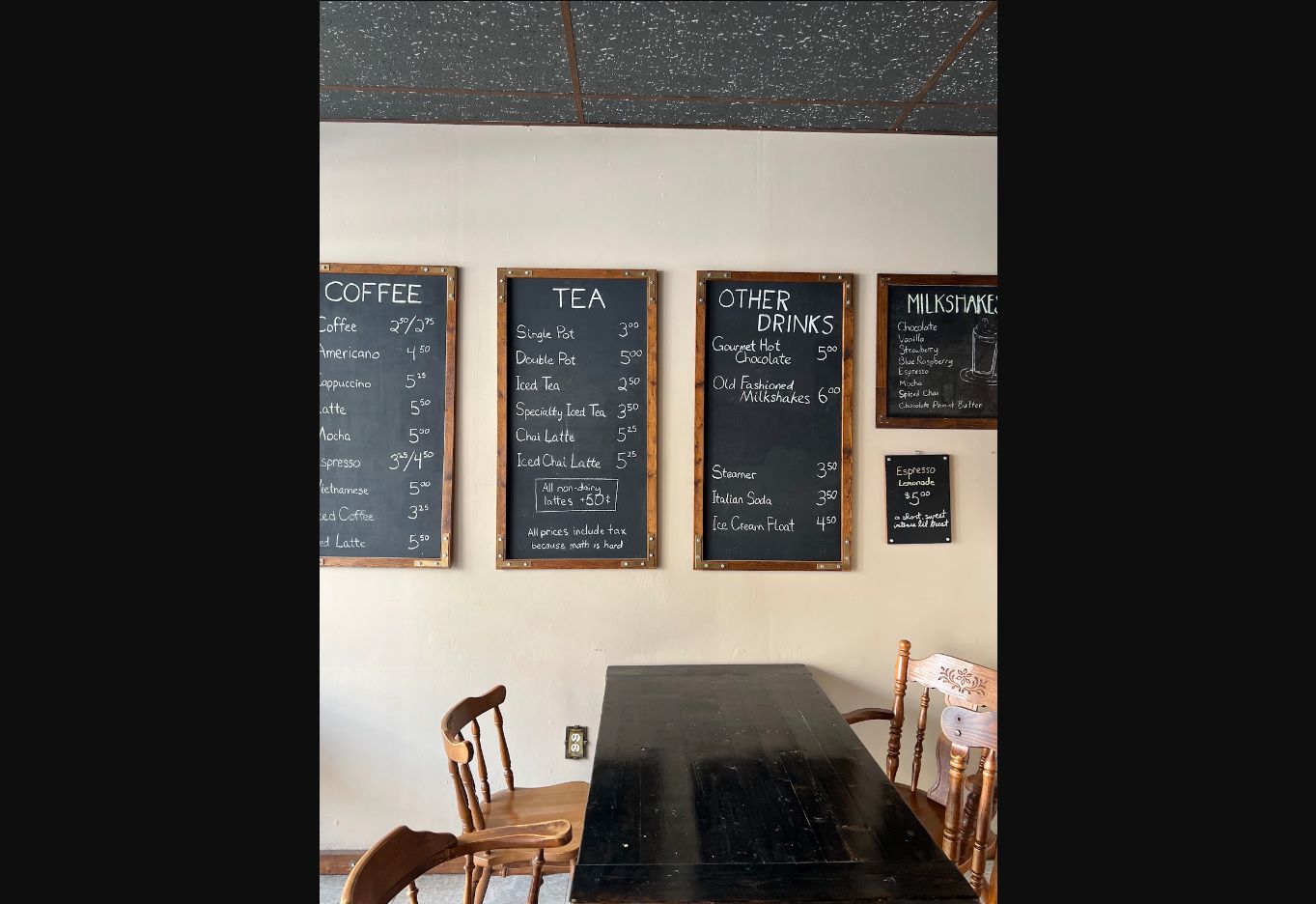 Wooden-framed chalkboards on a pale wall above a dark table and wooden chairs.