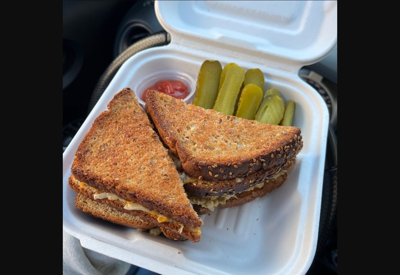 Toasted triangular sandwich halves in an open white takeaway container.